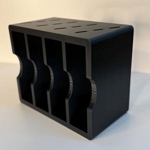May include: A black wooden knife block with a rectangular shape. The block has multiple slots on top for knife storage and curved cutouts on the sides. The block is designed to hold several knives.