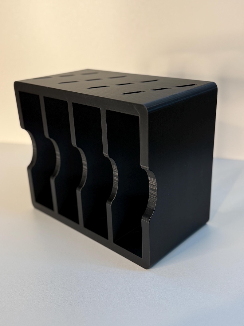 May include: A black wooden knife block with a rectangular shape. The block has multiple slots on top for knife storage and curved cutouts on the sides. The block is designed to hold several knives.
