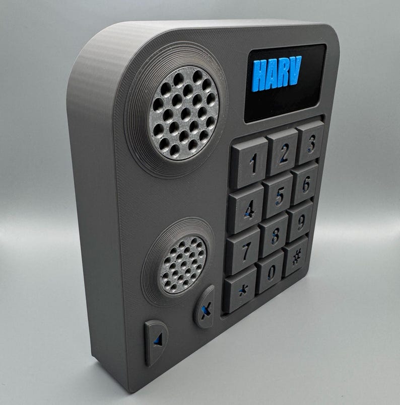 May include: A gray, rectangular device with a keypad, speakers, and the word "HARV" in blue. The keypad has numbers and symbols. The device has a retro, futuristic design.
