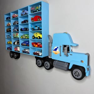 May include: A light blue, wall-mounted toy truck with multiple compartments filled with toy cars. The truck features a Dinoco logo and is designed to hold a collection of toy vehicles. The design is a fun and functional storage solution.