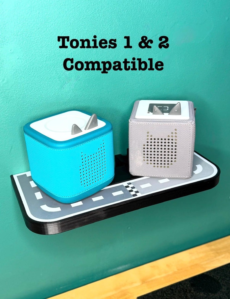 May include: Two Tonies audio players, one turquoise and one light purple, sit on a shelf designed as a road. The text "Tonies 1 & 2 Compatible" is above the players. The turquoise player has silver ears.