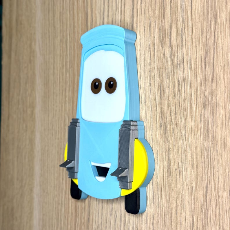 May include: A light blue wall-mounted object shaped like a cartoon vehicle with a white windshield featuring two brown eyes, a smiling mouth, yellow side accents, and two vertical grey rectangular components attached to the front surface.