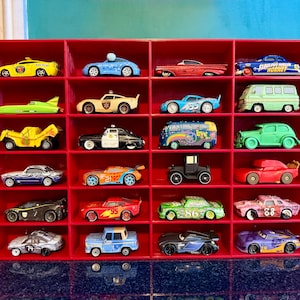 May include: A red display shelf filled with a collection of toy cars. The cars are various colors and styles, including a yellow taxi, a blue race car, and a green van. The shelf has 20 compartments.