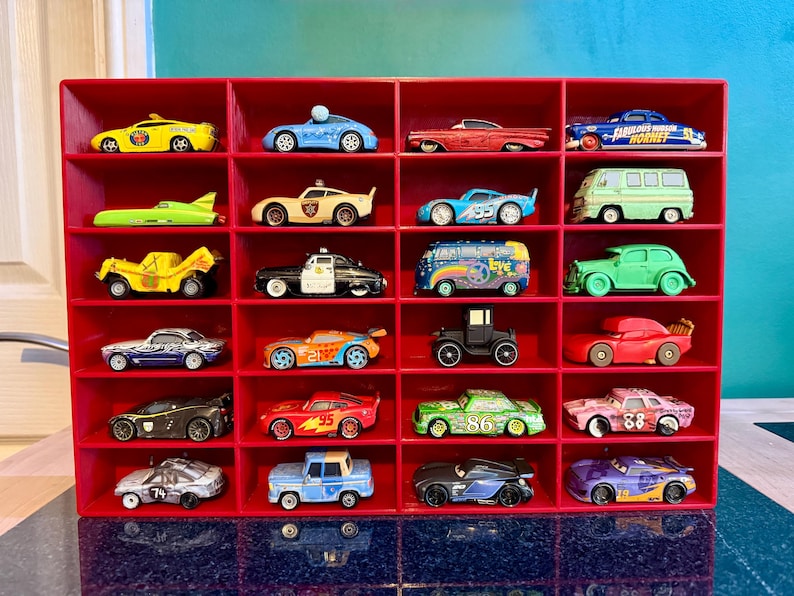 May include: A red display shelf filled with a collection of toy cars. The cars are various colors and styles, including a yellow taxi, a blue race car, and a green van. The shelf has 20 compartments.