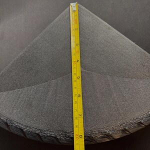 May include: A stack of dark gray, triangular fabric pieces. A yellow measuring tape shows the height of the stack is approximately 9 inches. The fabric appears to be a soft, textured material.