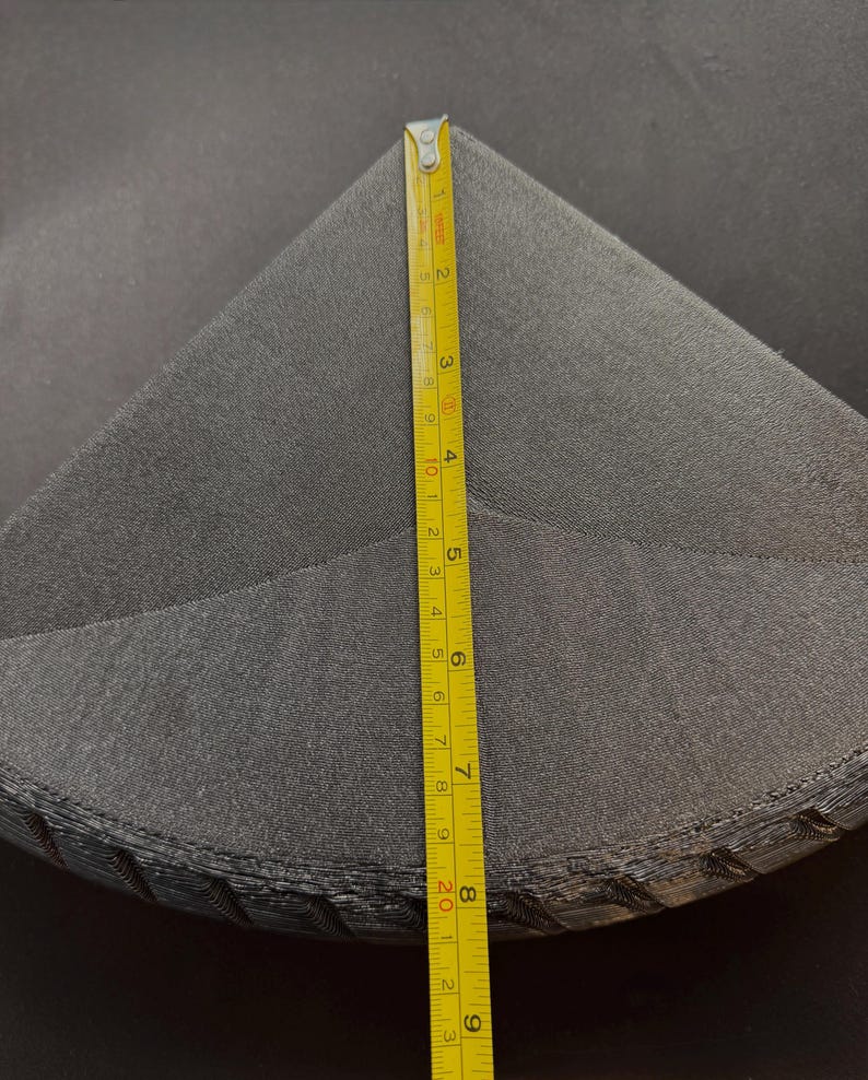 May include: A stack of dark gray, triangular fabric pieces. A yellow measuring tape shows the height of the stack is approximately 9 inches. The fabric appears to be a soft, textured material.