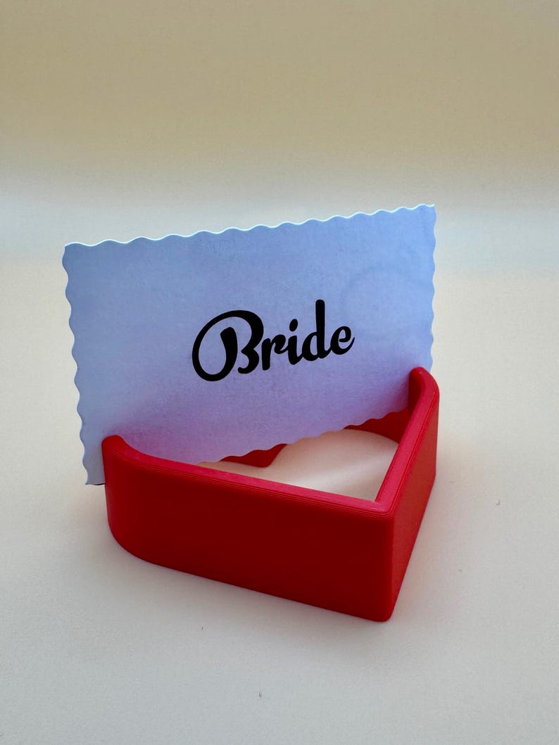 Red 3D-printed heart-shaped place card holder displaying a “Bride” card. Perfect for weddings, bridal showers, or receptions, this durable and elegant design adds charm to table settings and complements romantic themes for special events.