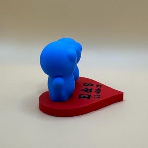 Cute 3D-printed cake topper featuring two blue figurines side by side on a red heart base engraved with initials and a date. Ideal for weddings, anniversaries, or events, this cute eco-friendly PLA decoration adds charm to any special occasion.