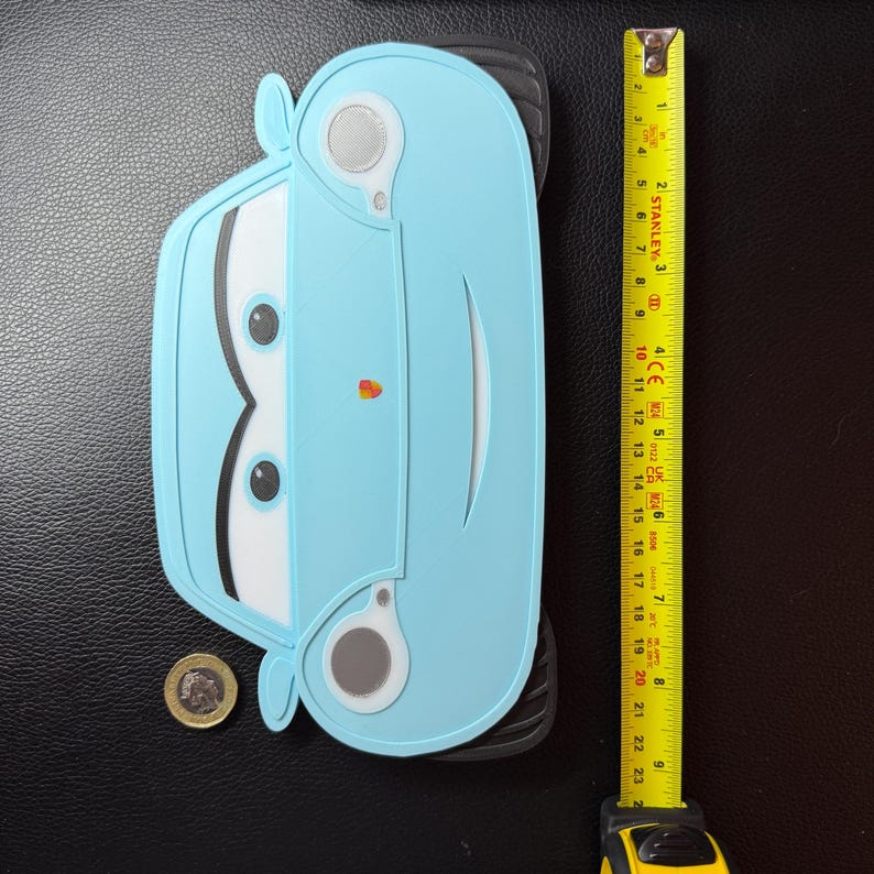 May include: A light blue car-shaped object with black tires and white and black details. A yellow tape measure shows the object is approximately 9 inches long. A coin is next to the car.