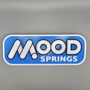 May include: A rectangular sign featuring the text "MOOD SPRINGS" in white, set against a blue backdrop. The sign has a white border and a textured finish, suitable for display indoors or outdoors.