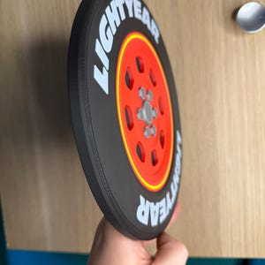May include: A black and red circular object with the text "LIGHTYEAR" in white. The object has a red center with a silver hub and is reminiscent of a tire.