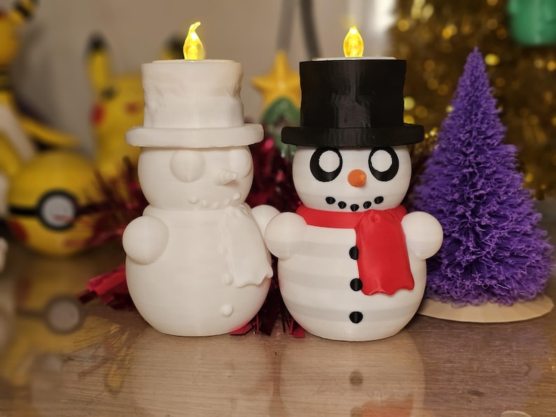 Adorable 3D-printed snowman tealight holders in white and multicolour, featuring festive designs with hats, scarves, and LED tealights. Perfect as Christmas decorations or gifts, displayed on a table with holiday-themed backdrops.