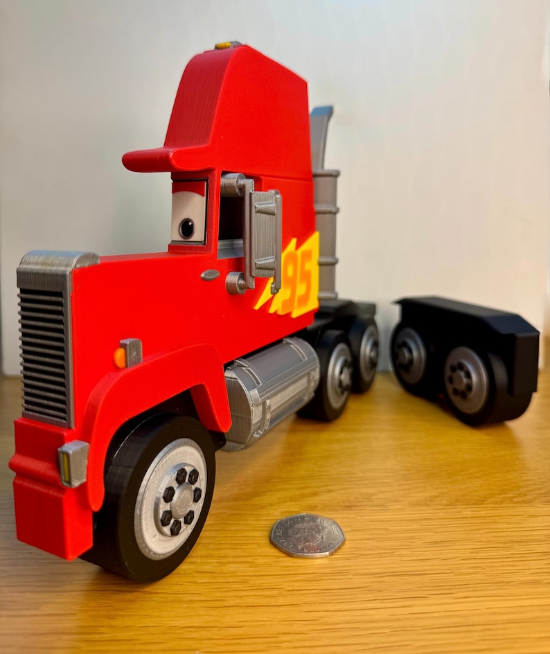 May include: A red toy semi-truck with a black trailer. The truck features a red cab with a visor, a silver grill, and the number "95" in yellow with a flame design. The wheels are black with silver rims. A coin is next to the truck.
