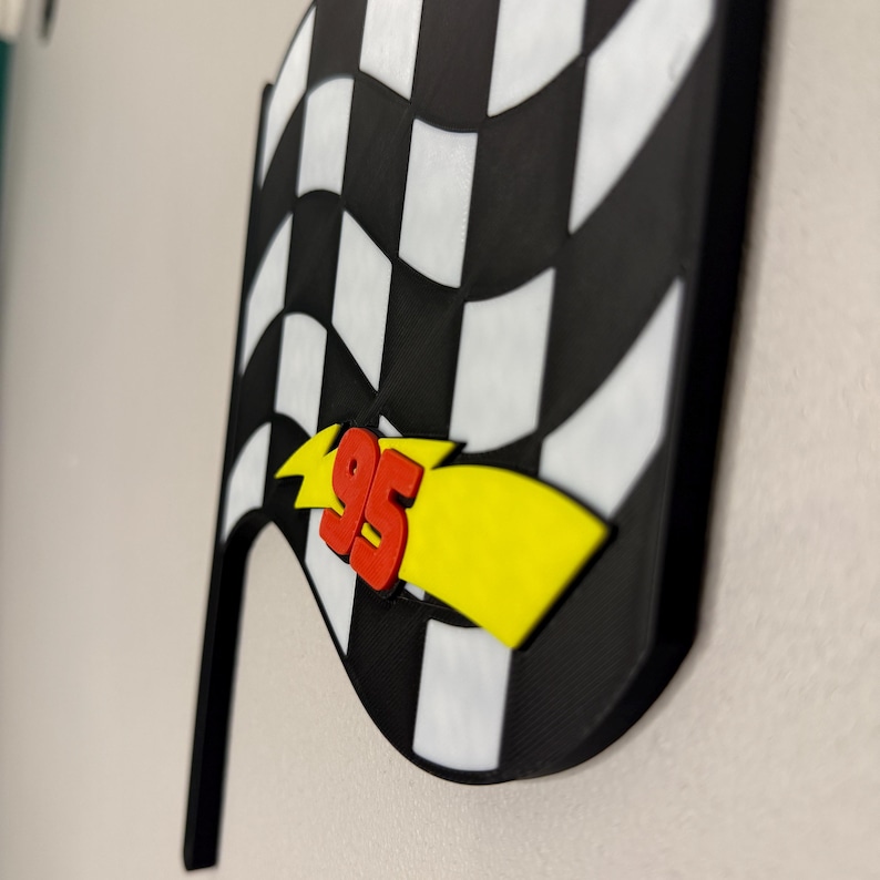 May include: A black and white checkered flag with a red "95" and yellow lightning bolt design. The flag has a black handle and is likely a decorative item or a party decoration.