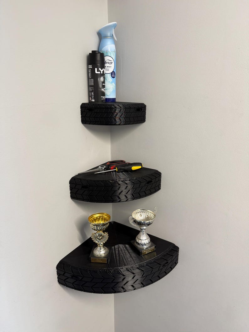 May include: Three-tiered corner shelves made from black tires. The top shelf holds a can of air freshener and a black spray bottle. The middle shelf has tools, and the bottom shelf displays two trophies.