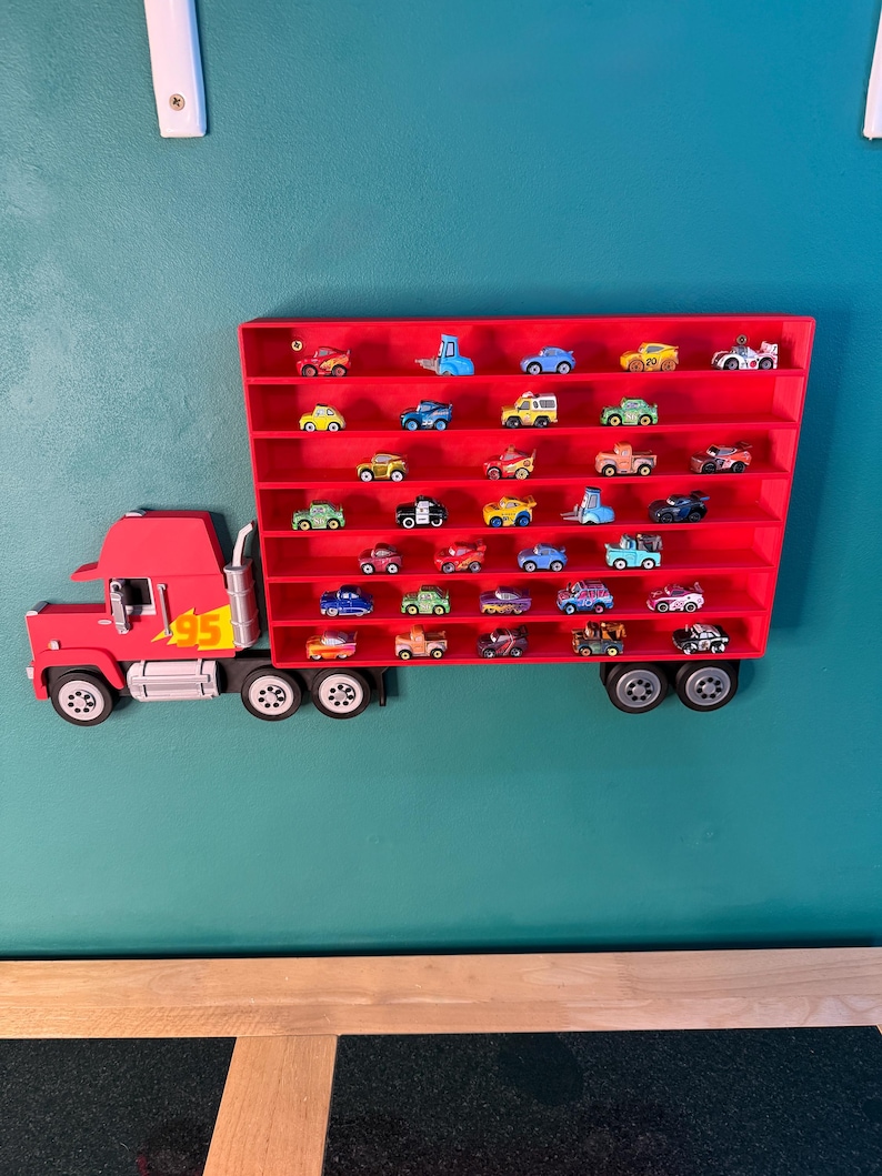 May include: A red wall-mounted display shelf shaped like a semi-truck with a trailer featuring multiple horizontal rows. The truck cab has a yellow lightning bolt graphic with the number 95. The trailer contains numerous small toy cars.