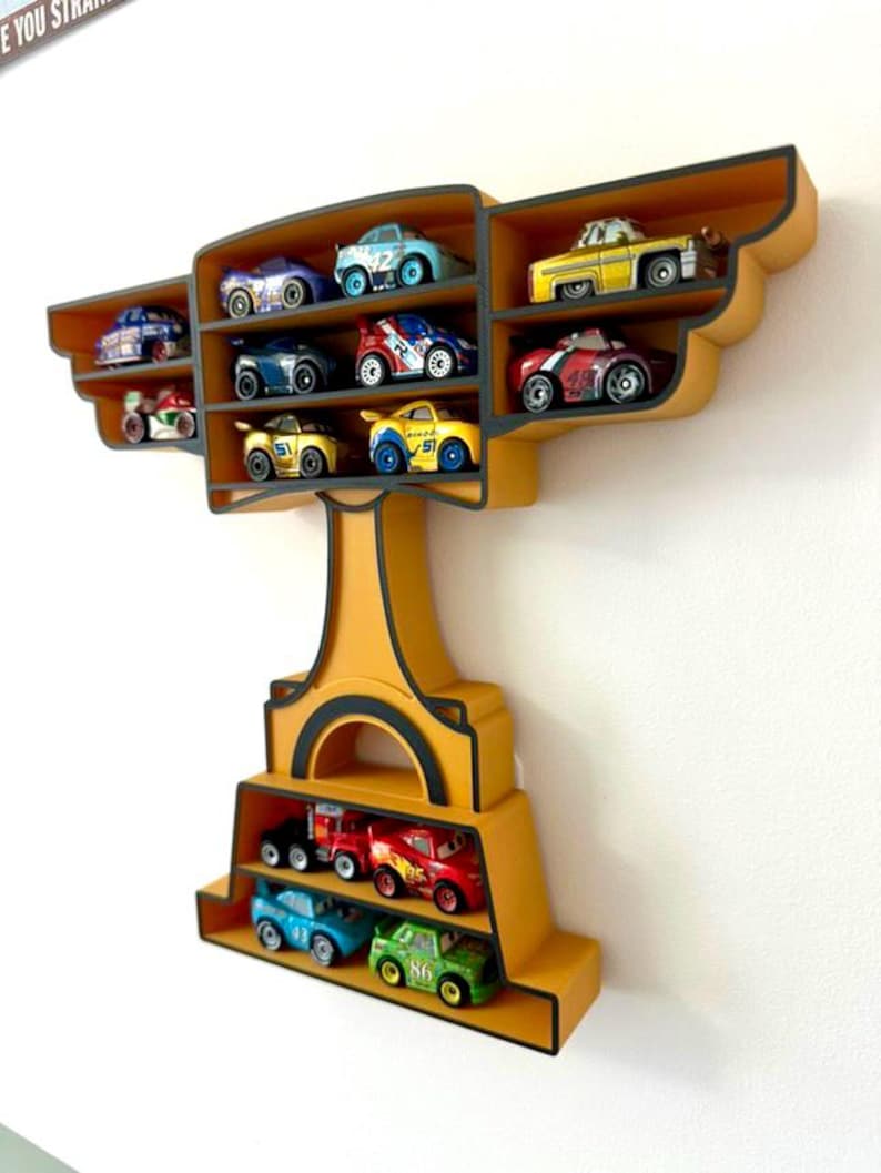 Puede incluir: Estanter&iacute;a de pared amarilla con forma de trofeo, llena de coches de juguete de varios colores. La estanter&iacute;a tiene m&uacute;ltiples compartimentos para exhibir los coches de juguete. Los coches son peque&ntilde;os y detallados, con diferentes dise&ntilde;os y n&uacute;meros.