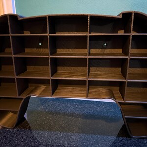 May include: A brown, multi-compartment shelf unit, resembling a video game controller. The unit has a series of small, square shelves, ideal for displaying small collectibles or organizing items. The overall design is modern and functional.