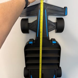 Op de afbeelding: Zwart en blauw Formule 1 raceauto-rek, ongeveer 107 cm hoog. Het rek heeft een strak ontwerp met meerdere compartimenten voor opslag. De auto heeft blauwe accenten en zwarte wielen, gemonteerd op een witte muur.