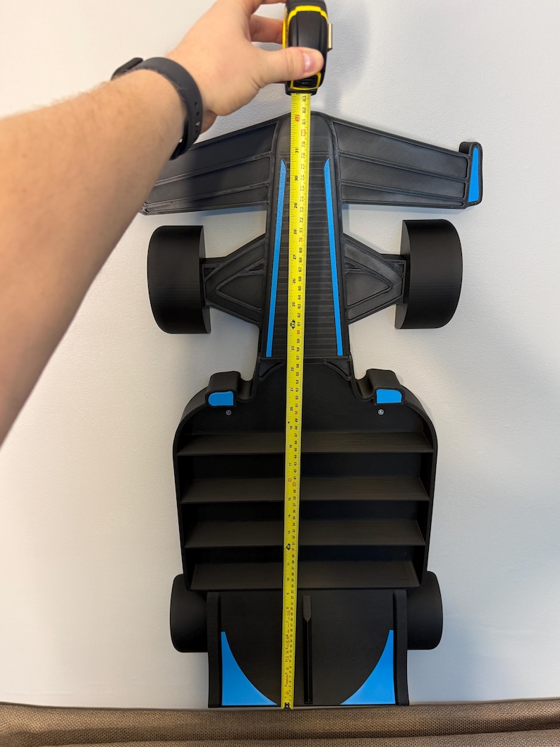 Op de afbeelding: Zwart en blauw Formule 1 raceauto-rek, ongeveer 107 cm hoog. Het rek heeft een strak ontwerp met meerdere compartimenten voor opslag. De auto heeft blauwe accenten en zwarte wielen, gemonteerd op een witte muur.