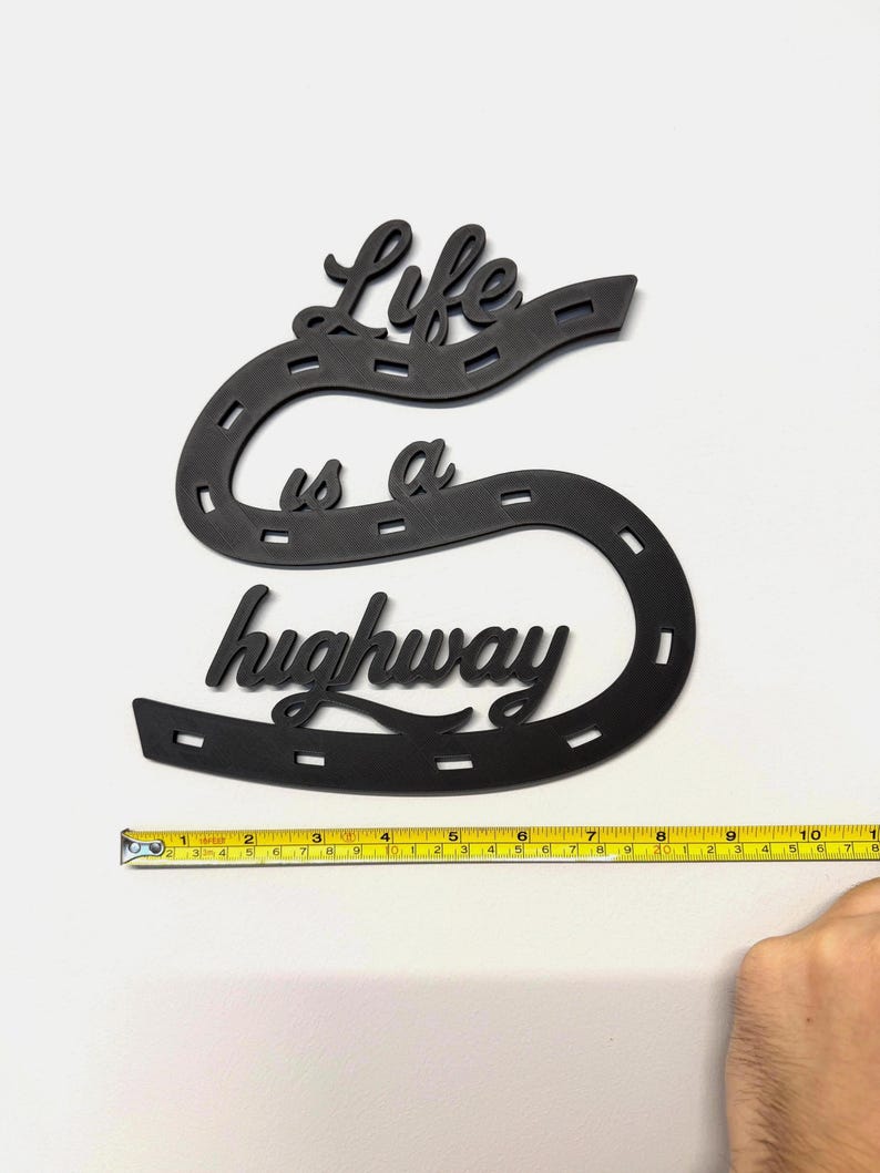 May include: Black wooden wall art in the shape of a large letter "S" with the words "Life is a highway" cut out. The art piece is approximately 11 inches long. The design resembles a road.