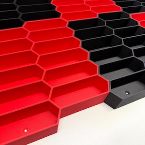 May include: A modular storage system featuring a repeating hexagonal grid pattern. The structure consists of interconnected open-top bins in alternating solid red and matte black colors, each with a small circular mounting hole at the base.