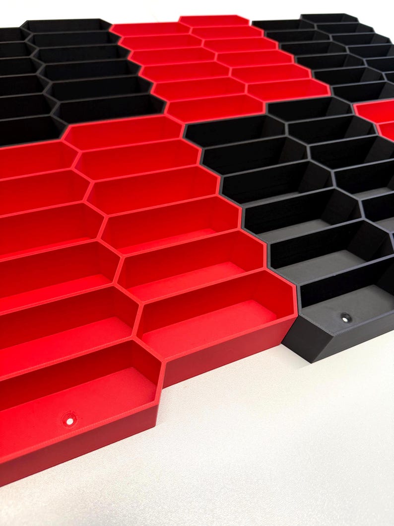 May include: A modular storage system featuring a repeating hexagonal grid pattern. The structure consists of interconnected open-top bins in alternating solid red and matte black colors, each with a small circular mounting hole at the base.