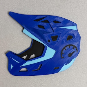 May include: A blue and light blue full-face helmet with a speedometer graphic. The helmet has a visor and several ventilation openings. The design is a combination of dark and light blue, with black accents.