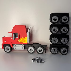 May include: A red and black toy truck with the number "95" in yellow. The truck has a silver exhaust pipe and wheels. There are three stacks of black wheels and several silver cylinders next to the truck.