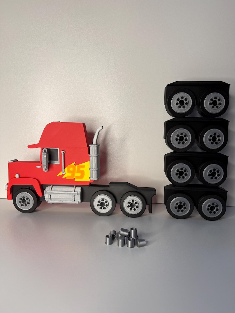 May include: A red and black toy truck with the number "95" in yellow. The truck has a silver exhaust pipe and wheels. There are three stacks of black wheels and several silver cylinders next to the truck.