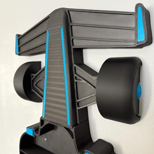 Op de afbeelding: Zwart en grijs wandrek in de vorm van een Formule 1-raceauto. Het rek heeft een achtervleugel, wielen en blauwe accenten. Ontworpen om kleine items in op te bergen.