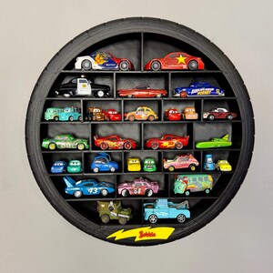 May include: A black, circular shelf made from a tire, filled with toy cars of various colors and designs. The shelf has multiple compartments, each holding a different car. The word "Bubble" is visible on a yellow arrow-shaped sign.