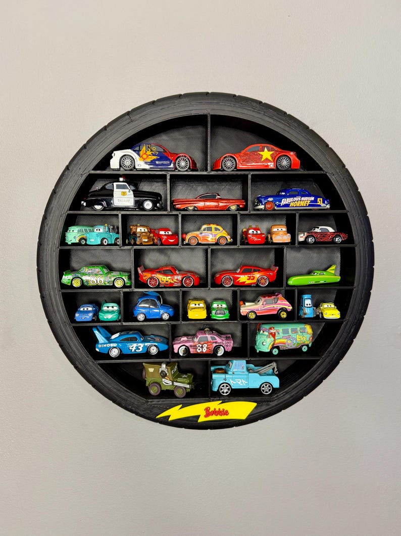 May include: A black, circular shelf made from a tire, filled with toy cars of various colors and designs. The shelf has multiple compartments, each holding a different car. The word "Bubble" is visible on a yellow arrow-shaped sign.