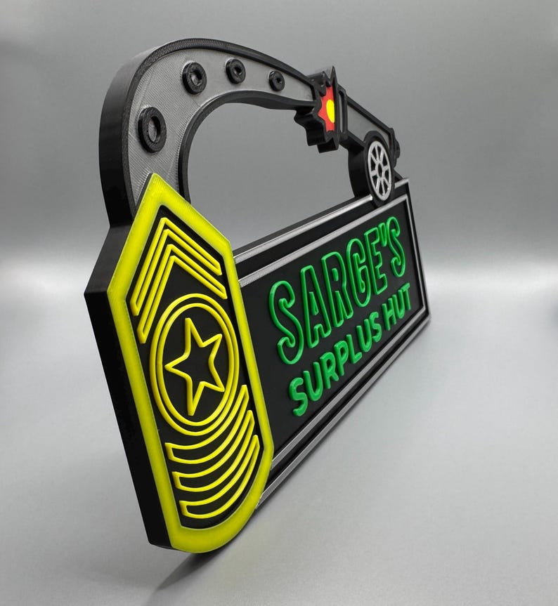 May include: A 3D-printed sign with the text "SARGE'S SURPLUS HUT" in green on a black background. The sign has a yellow and black military insignia and a black and gray handle with a small vehicle design. The sign is approximately 12 inches long.