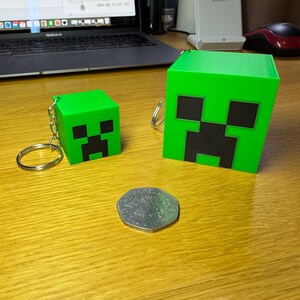 3D printed Minecraft creeper head keychains keyrings in bright green with pixelated black faces, available in two sizes: small (3cm) and large (5cm). Perfect for gamers or as a unique gift for fans of Minecraft.
