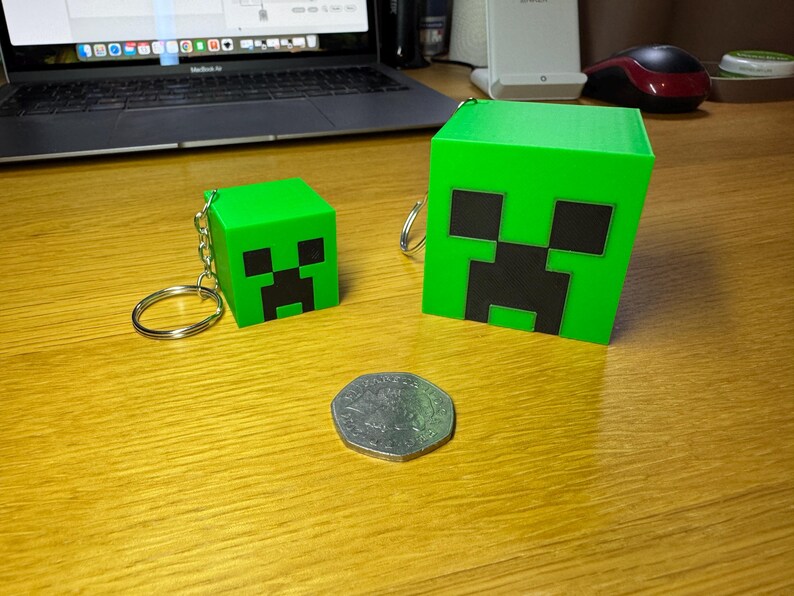 3D printed Minecraft creeper head keychains keyrings in bright green with pixelated black faces, available in two sizes: small (3cm) and large (5cm). Perfect for gamers or as a unique gift for fans of Minecraft.