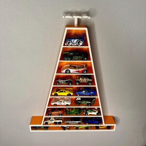 May include: A wall-mounted display shelf in the shape of a cone, coloured orange and white, filled with toy cars. The shelf has multiple levels to showcase the miniature vehicles. The cars are in different colours and styles.