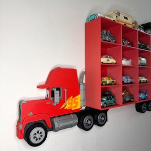 May include: A red truck-shaped wall shelf with multiple compartments, filled with toy cars. The truck features a red cab with the number "95" and a lightning bolt graphic. The shelf is designed to resemble a semi-truck trailer.