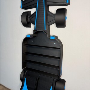 Op de afbeelding: Zwart en blauw Formule 1 raceauto-vormig wandrek. Het rek heeft een strak ontwerp met blauwe accenten op de vleugels en wielen. Het heeft meerdere planken voor display of opslag, gemonteerd op een witte muur.