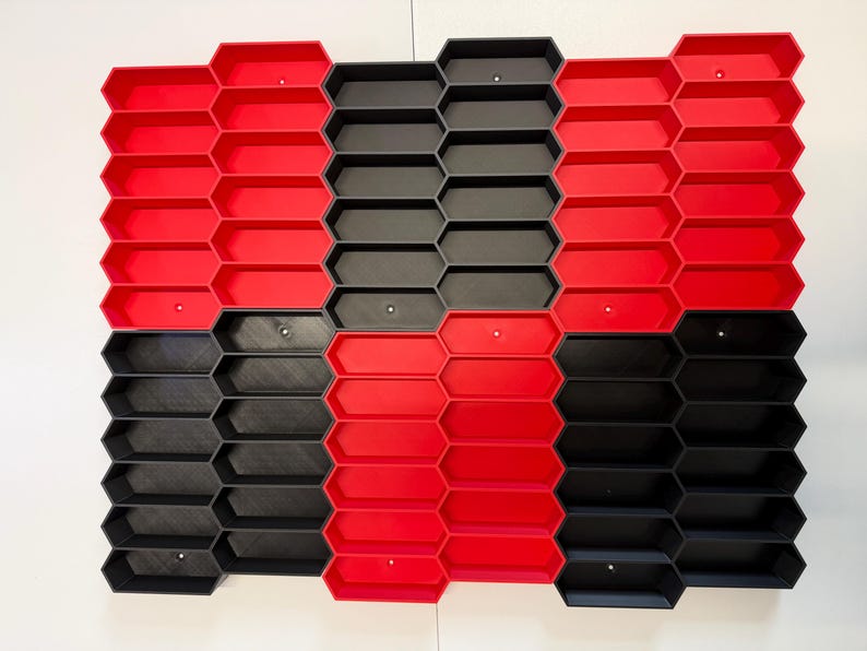 May include: A modular wall-mounted storage system featuring a grid of interlocking hexagonal compartments. The unit is composed of alternating red and black plastic sections, creating a geometric pattern with open-front bins for organization.