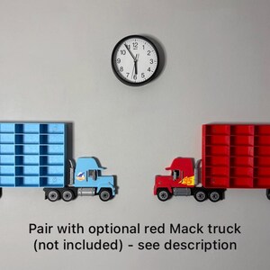 May include: Two toy semi-trucks, one light blue and one red, are displayed against a gray background. The blue truck has a blue grid-like trailer, and the red truck has a red grid-like trailer. A black clock hangs above the trucks.