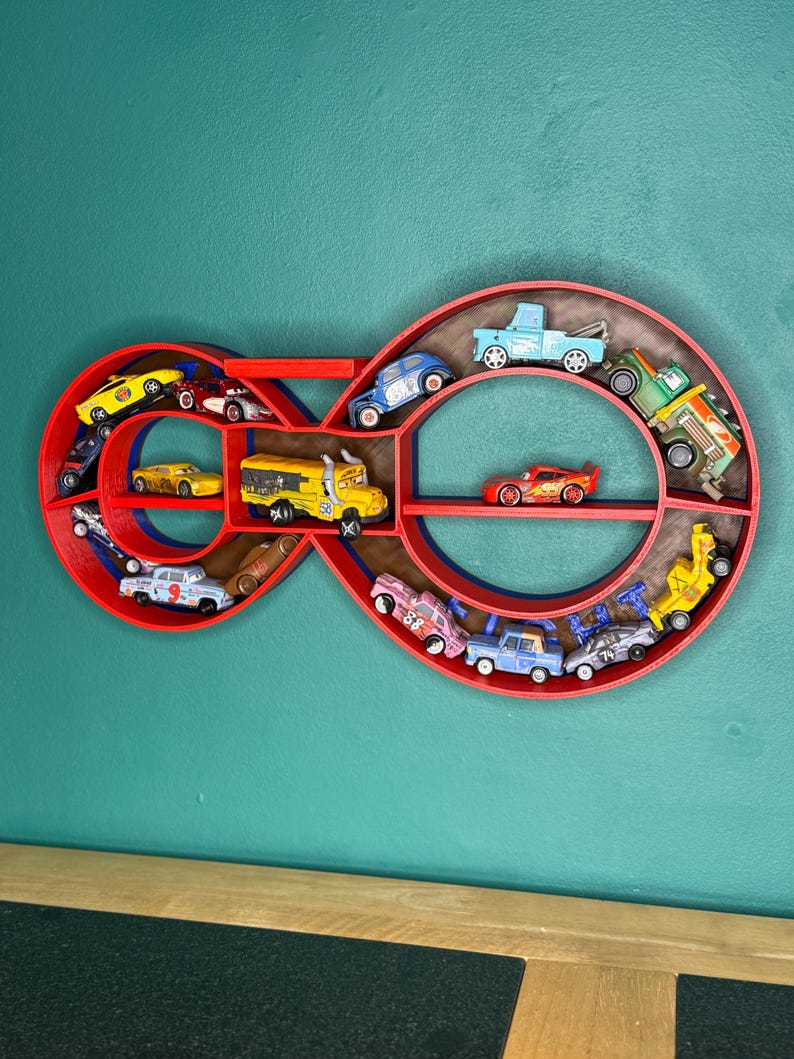 May include: A red infinity-shaped shelf filled with toy cars of various colors. The shelf is mounted on a teal wall. The toy cars include a yellow school bus, a red race car, and several other vehicles.