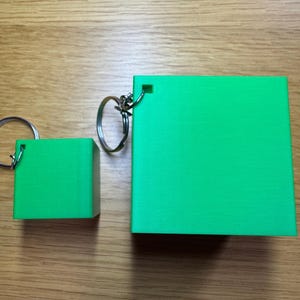 3D printed Minecraft creeper head keychains keyrings in bright green with pixelated black faces, available in two sizes: small (3cm) and large (5cm). Perfect for gamers or as a unique gift for fans of Minecraft.