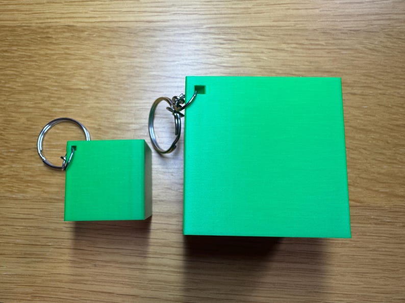 3D printed Minecraft creeper head keychains keyrings in bright green with pixelated black faces, available in two sizes: small (3cm) and large (5cm). Perfect for gamers or as a unique gift for fans of Minecraft.