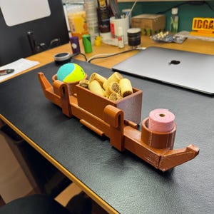 Side view of PETG 3D-printed dog crate organiser in wood effect. Holds treats, a tennis ball, and poo bags with slots for two leads. Heat-resistant and tool-free with adjustable hooks. Customisable with dog names and also available in black.