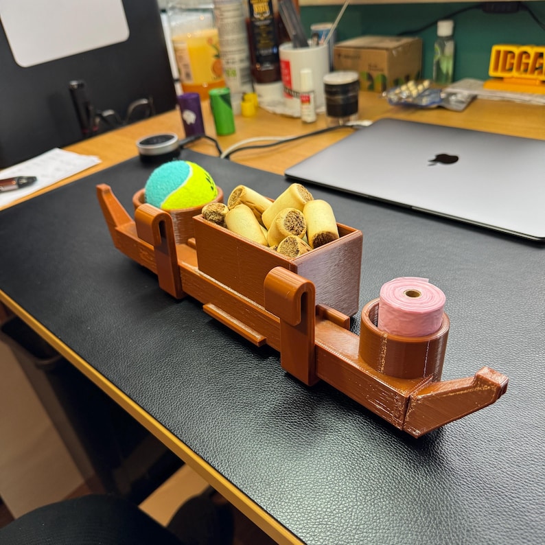 Side view of PETG 3D-printed dog crate organiser in wood effect. Holds treats, a tennis ball, and poo bags with slots for two leads. Heat-resistant and tool-free with adjustable hooks. Customisable with dog names and also available in black.