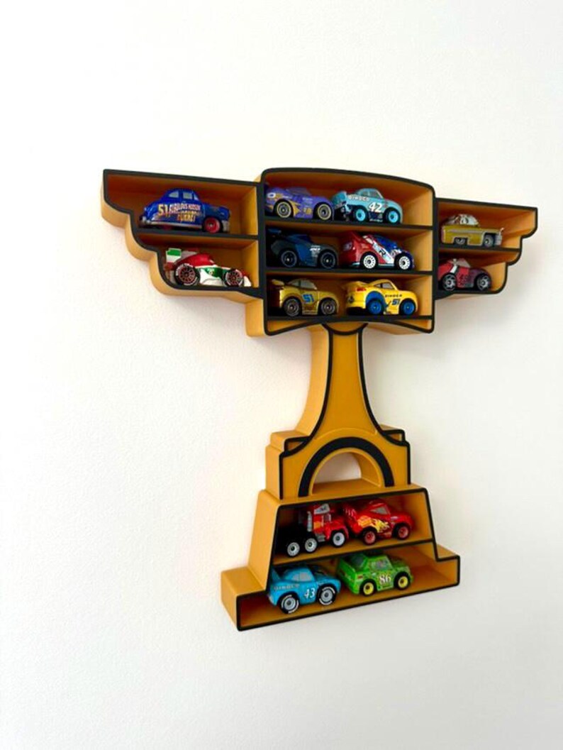 Puede incluir: Estanter&iacute;a de pared amarilla con forma de trofeo con m&uacute;ltiples compartimentos, cada uno con una colecci&oacute;n de coches de carreras de juguete. La estanter&iacute;a tiene un borde negro y est&aacute; montada en una pared blanca. Los coches son de colores brillantes.