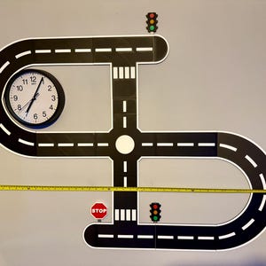 May include: A black and white road play set with a clock, stop sign, and traffic lights. The road measures approximately 48 inches in length. The clock shows the time is 1:00.