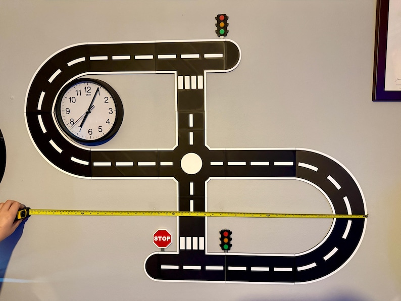 May include: A black and white road play set with a clock, stop sign, and traffic lights. The road measures approximately 48 inches in length. The clock shows the time is 1:00.