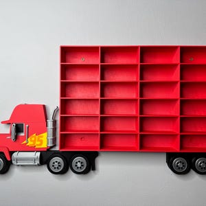May include: A red truck-shaped wall shelf with multiple compartments. The truck cab features a yellow '95' graphic with a flame design. The shelf is mounted on a light gray wall, offering a playful storage solution.